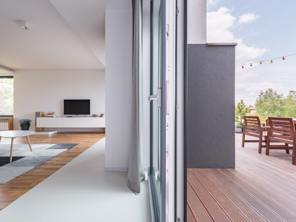 Modern UK home with sliding glass doors connecting a bright living room to a timber-decked outdoor seating area under blue skies