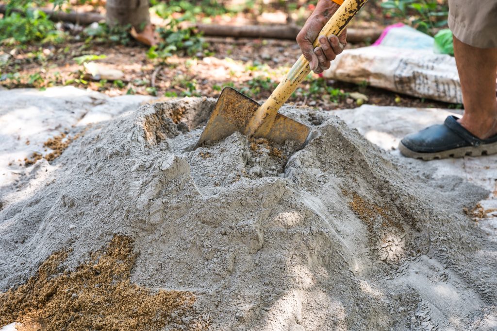 Worker mixing sand and cement with a shovel on-site, preparing building materials for construction work